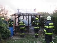 Dohořívající chata a hasiči, kteří zbytky požáru hlídají